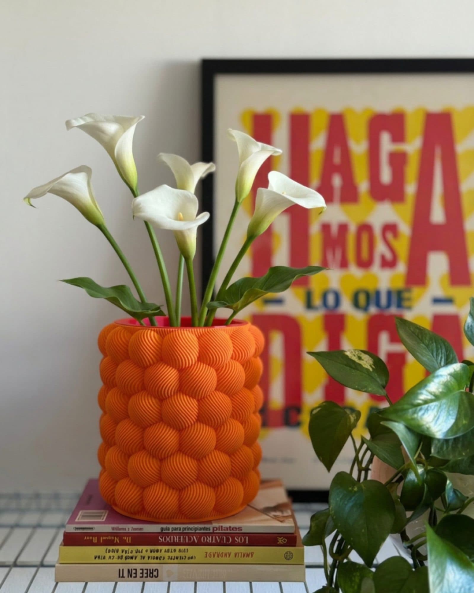 Jarrón Casemira naranja con calas blancas frente a un cartel tipográfico