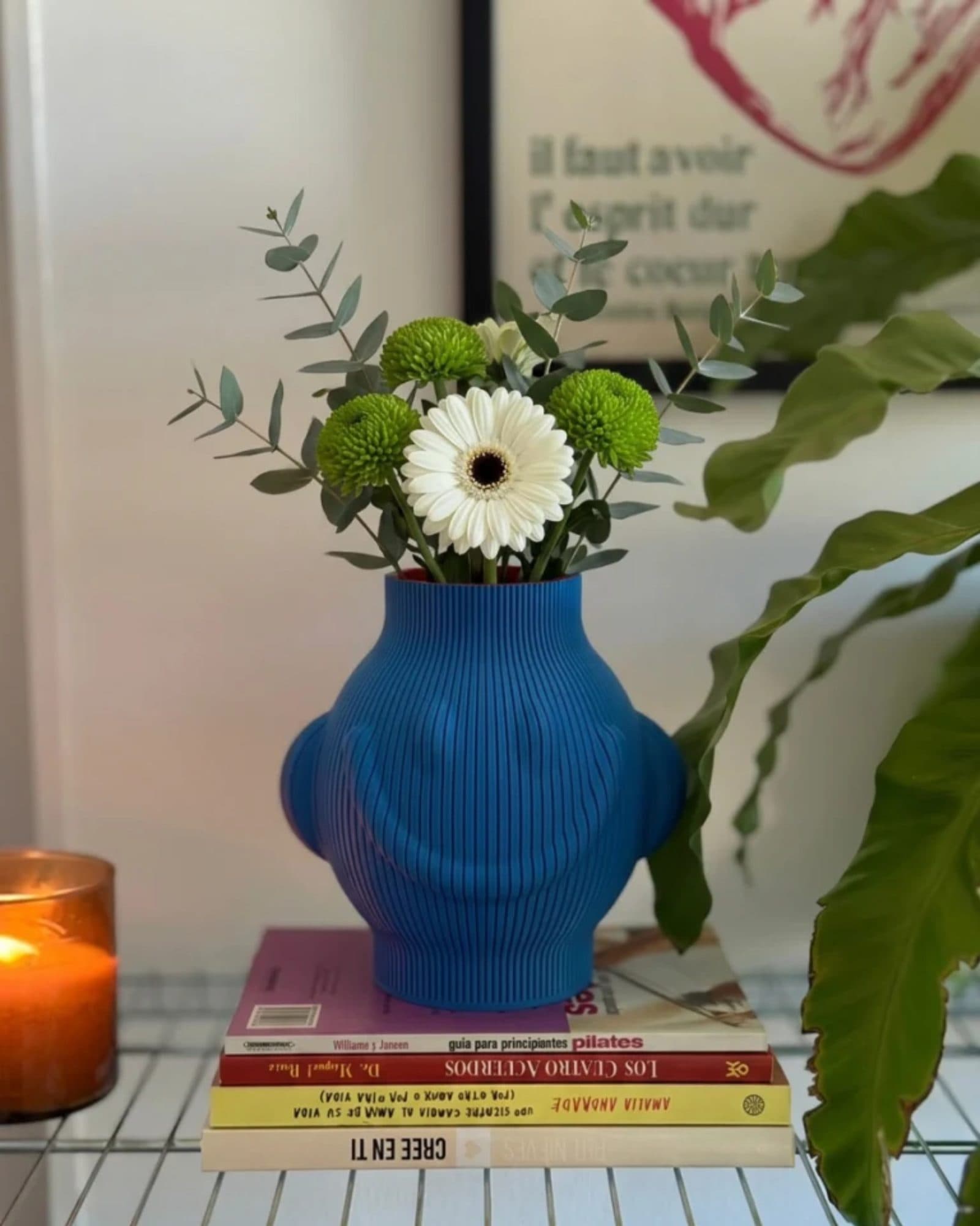 Jarrón Pepe azul con margaritas y eucalipto sobre una pila de libros